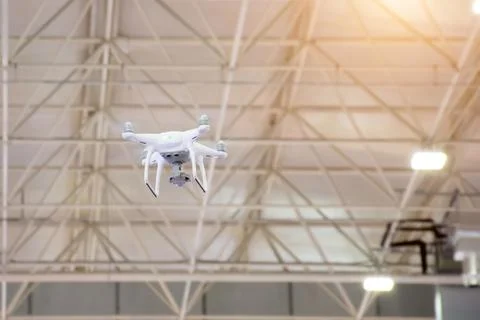 White drone in motion flying from the ceiling inside the building. Stock Photos