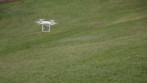 White drone quadcopter flying in the blue sky on the background of the grass Stock Footage 76967438