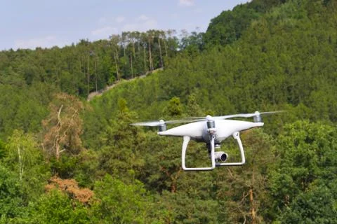 White drone quadrocopter with camera flying over forest Stock Photos