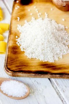 White dry rice over kitchen board with some vegetables and pasta around. Stock Photos