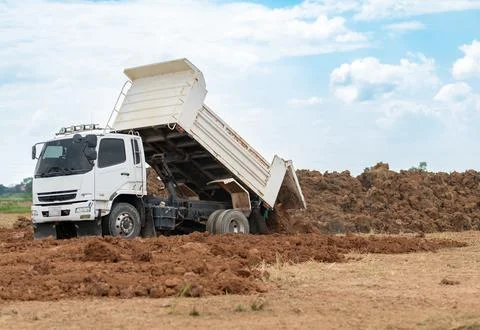 White dump truck unloading soil and dirt at an outdoor construction site or.. Photos