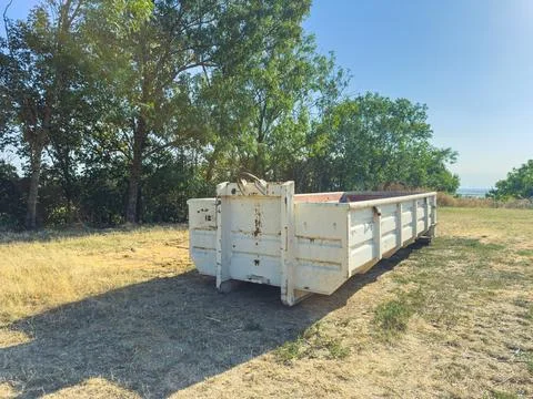 White dumpster located in an open area surrounded by trees on a sunny day Stock Photos