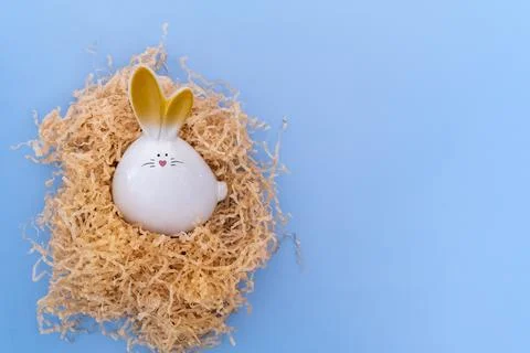 A white Easter bunny with an egg sitting in a homemade nest on a blue backgro Stockfoto's