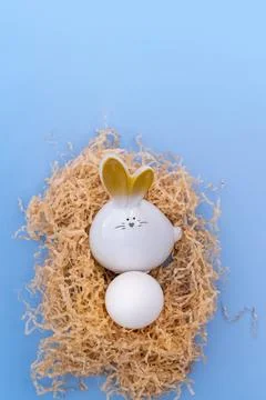 A white Easter bunny with an egg sitting in a homemade nest on a blue backg.. Stock Photos