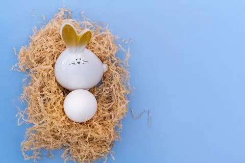 A white Easter bunny with an egg sitting in a homemade nest on a blue backg.. Stock Photos