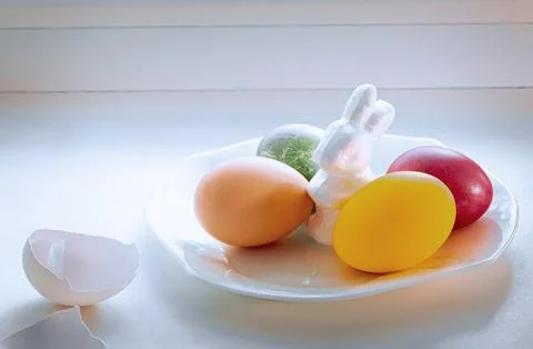 A white Easter bunny next to Easter eggs stand on a white plate on the wind.. Stock Photos