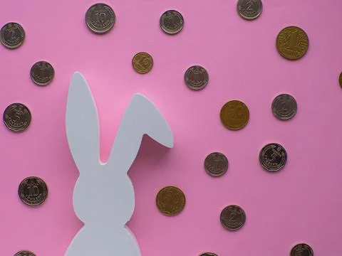 White Easter bunny surrounded by coins on pink background. Stock Photos