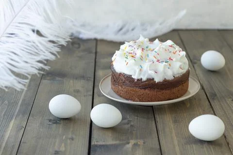 White Easter cake with colored sweet sprinkles near eggs and feathers on a wo Stock Photos