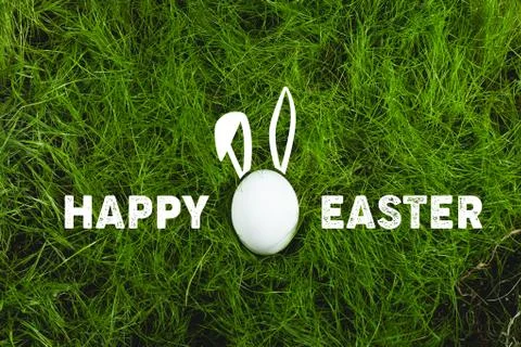 White Easter egg with bunny ears on green grass with inscription Happy Easter Foto stock