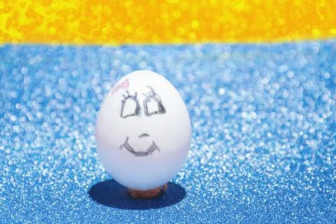 White Easter egg with a painted face with a smile on a blue and yellow bright ba Stock Photos