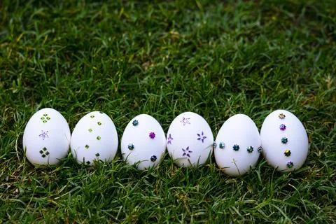 White Easter eggs adorned with colorful sequins and arranged On Green Grass Foto stock