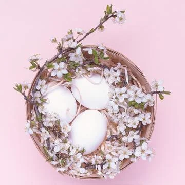 White easter eggs in a basket with flowers on a pink background. Square photo Stock Photos