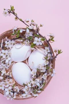 White easter eggs in a basket with flowers on a pink background. Vertical pho Stock Photos