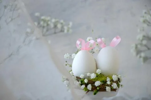 White Easter eggs with pink bunny ears in nest with white small flowers thr.. Stock Photos