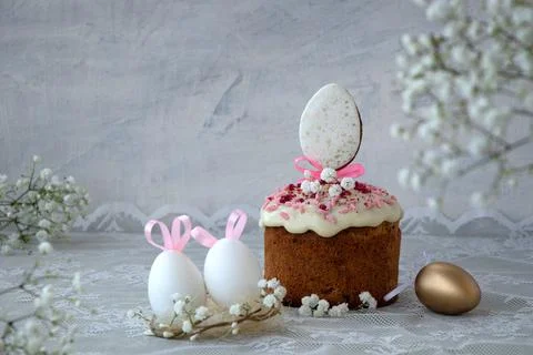 White Easter eggs with pink rabbit or bunny ears in nest next to Easter cak.. Stock Photos