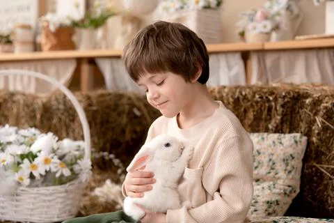 White Easter rabbit sits on the hands of a little boy, who huggs the rabbit Stock Photos