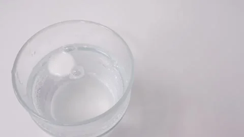 White effervescent tablet dissolving in a transparent glass of water on a w.. Stock Footage 335141472