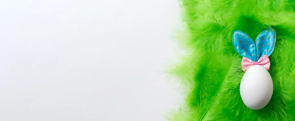 White egg with Easter Bunny ears on a green soft gentle feather background, c Foto stock