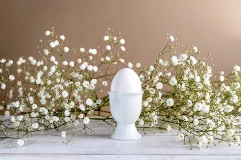 White egg in egg cup and spring flowers, gypsophila, on a wooden background and Stock Photos