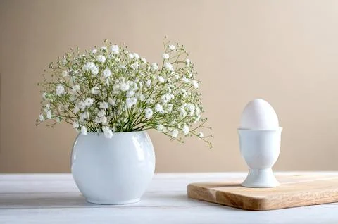 White egg in egg cup and gypsophila in white vase on light background. Easter Stock Photos