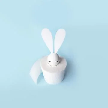White egg with hare ears in a roll of toilet paper. Hard shadow on a light Stock Photos