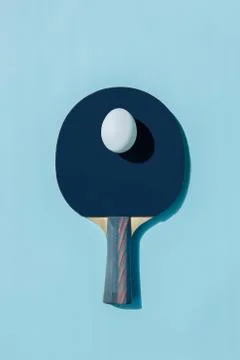 A white egg lies on a blue ping pong racket. A shadow falls from the egg. Stock Photos
