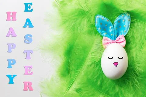 A white egg with a painted face and ears of an Easter Bunny on a green soft g Foto stock