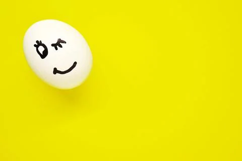 White egg with painted smiling face on yellow background Stock Photos