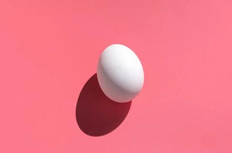 A white egg on a pink background with a hard shadow. Minimalistic nutrition. Stock Photos