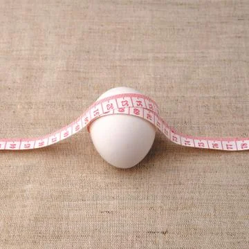 A white egg is wrapped with a measuring centimeter. Stock Photos