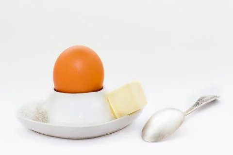 White eggcup with brown egg, spoon and butter with salt Stock Photos