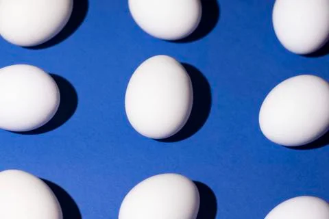 White eggs are located on the edge and in the center of the blue background Stock Photos