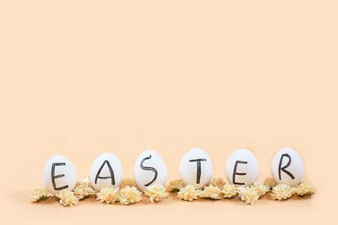 White eggs with black letters EASTER around flowers on yellow background. Stock Photos