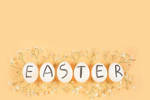 White eggs with black letters EASTER around Gypsophila flowers on yellow Foto stock