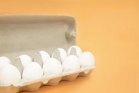 White eggs in an egg carton on an orange background. Place for text. copy space Stock Photos