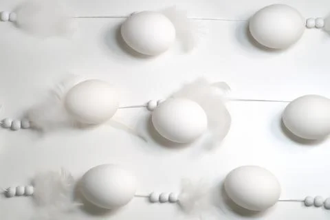 White eggs lie in a row on strings with beads and feathers on a white backgro Stock Photos