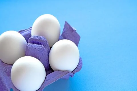 White eggs in a package on a blue background close-up view from above. Stock Photos