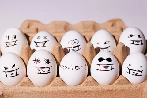 White eggs with painted faces in a box on a light background Stock Photos
