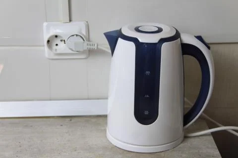 White electric kettle stands on a gray table plugged into a power outlet Foto stock