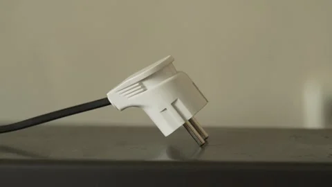 White electric plug with a black cord resting on a surface. 스톡 동영상 341243709
