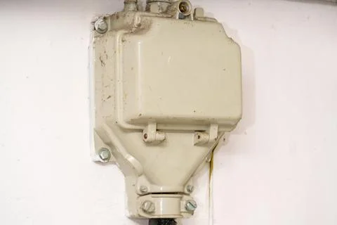 White electrical box mounted on a wall near wiring, showing signs of wear a.. Stock Photos