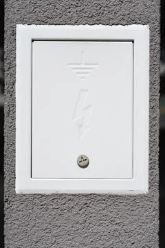 White electrical grounding box door mounted on a gray concrete wall Stock Photos