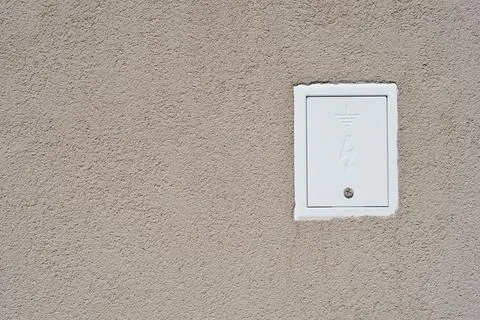 White electrical grounding box door mounted on a beige wall 库存照片