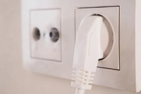 White electrical plug connected to a wall socket in a home Stock Photos