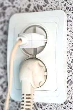 White electrical plug in the electric socket on wall. Connected ac plugs. Stock Photos