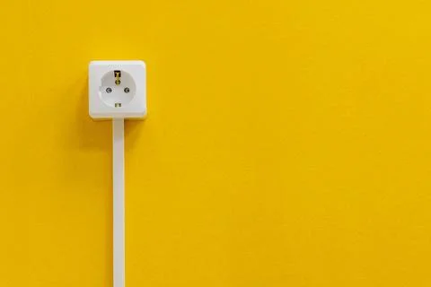 A white electrical socket is affixed to a bright yellow wall Stock Photos