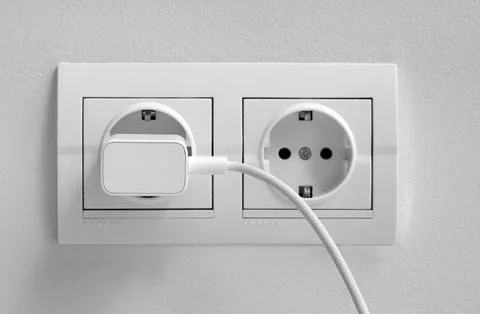 White electrical wall outlet with plugged-in charger and cable, modern power  Stock Photos