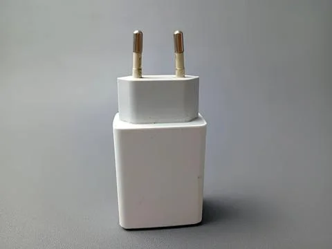 White electronic power adapter with two prongs on gray background Stock Photos