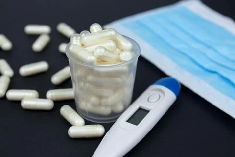 White electronic thermometer with packs of tablets and blue medical face mask Foto stock