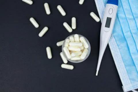 White electronic thermometer with packs of tablets and blue medical face mask Stock Photos